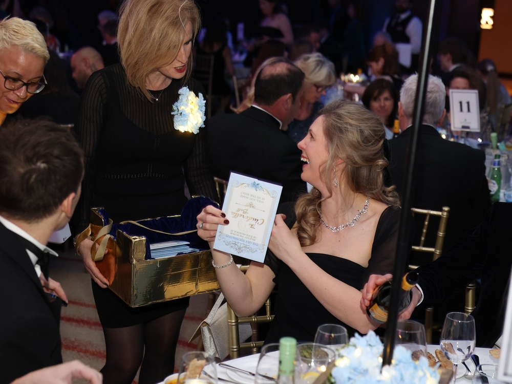 A guest sitting at their table at the Lily ball buying a raffle entry from a volunteer