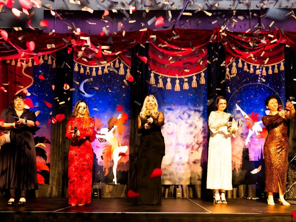A group of people standing on the stage at The Lily ball holding confetti cannons