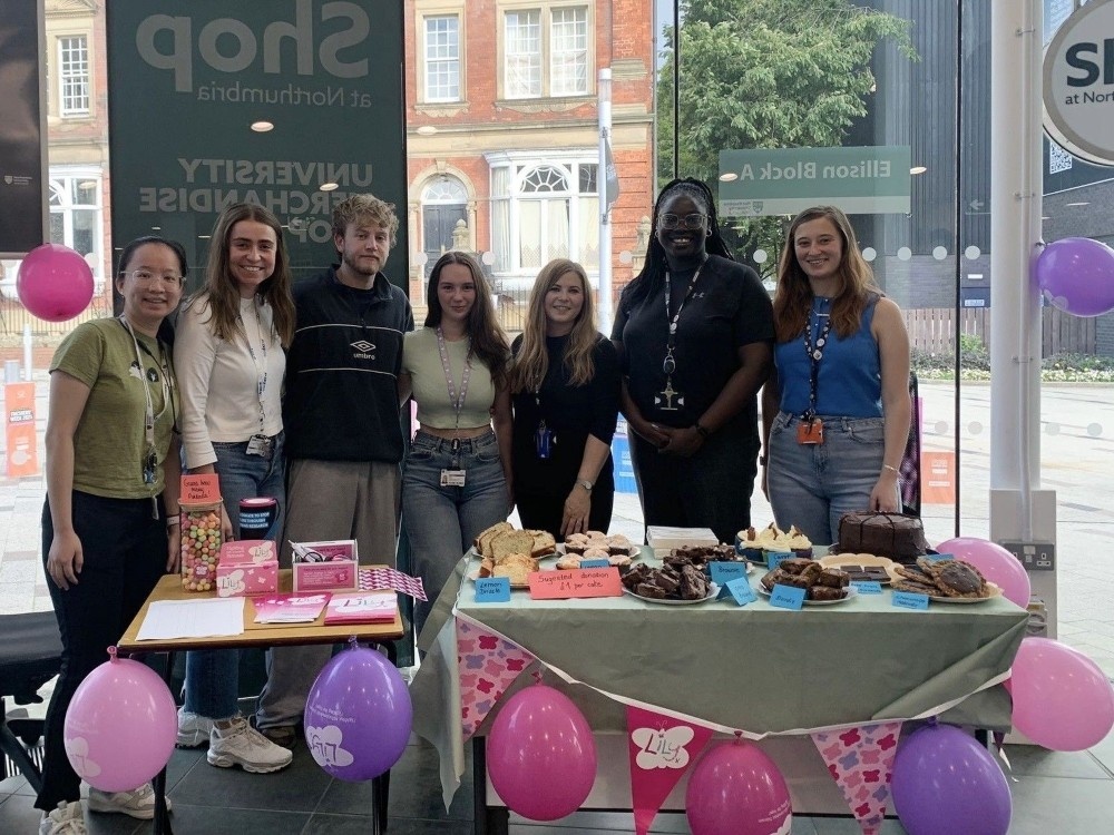 A group of people behind an awareness stand for mito week filled with balloons, bunting and cakes
