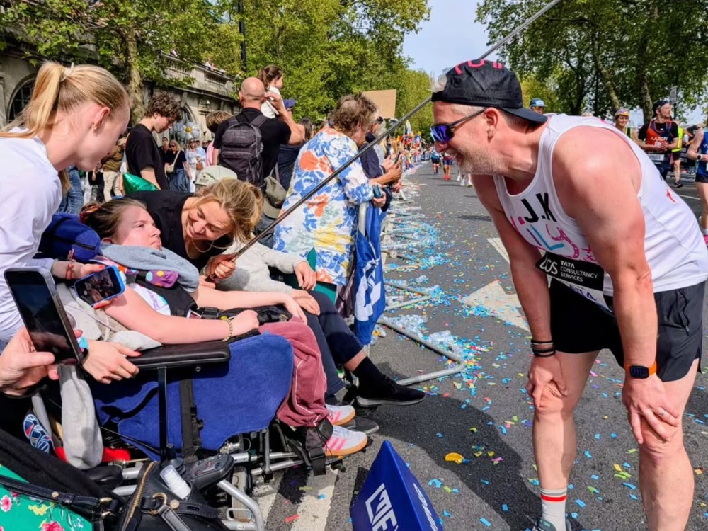 A man in a Lily top running the marathon stopping at the side of the road to speak to his family