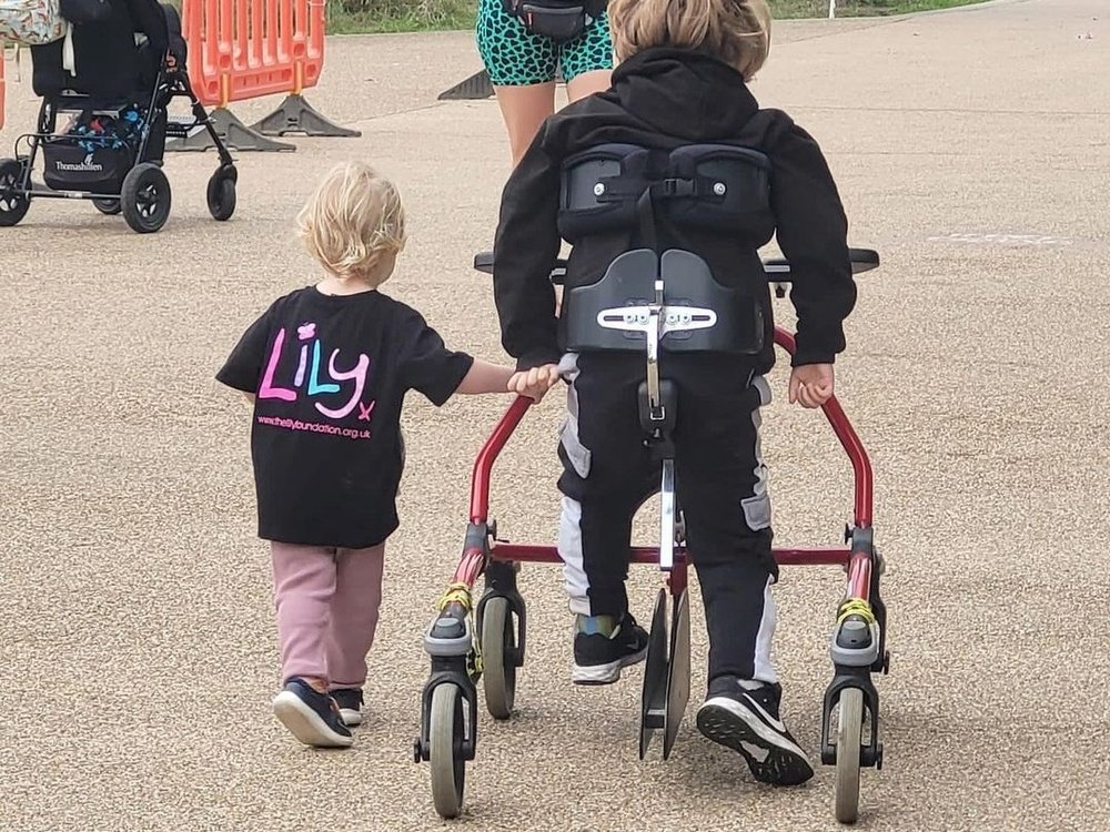Butterfly Run 2025 - A young mito warrior walking along on his walker at the Butterfly Run with his younger sibling