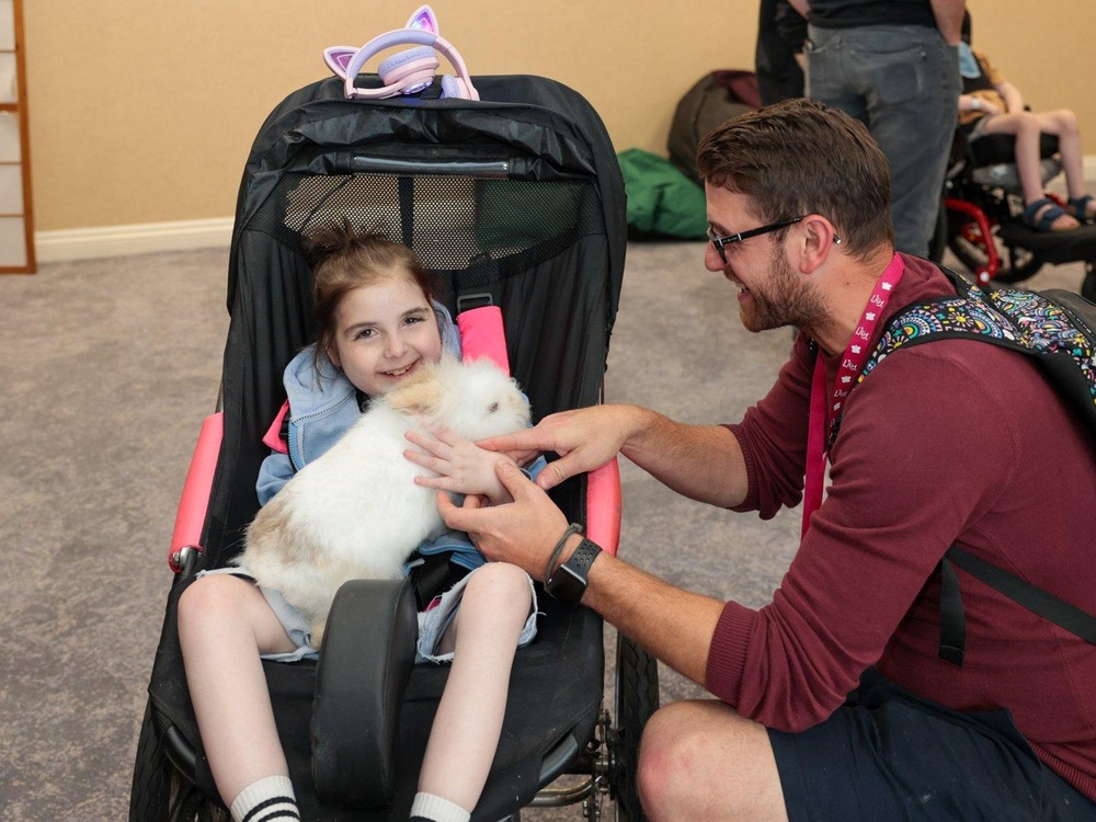 A young girl in a buggy holds a fluffy white rabbit while a man leans over to help
