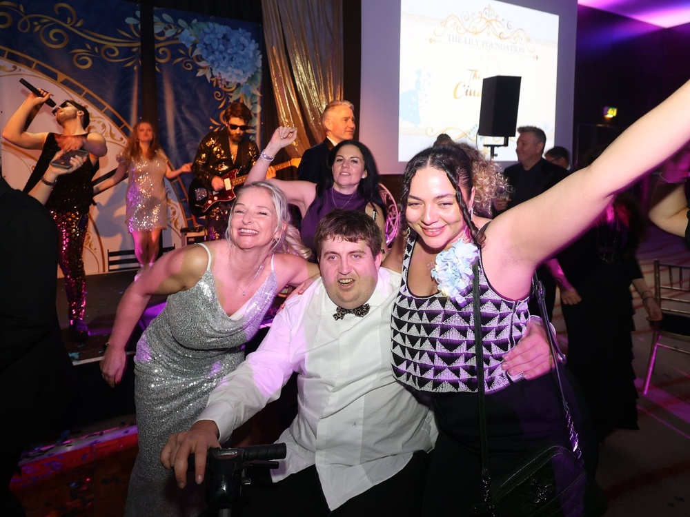 Adult mito patient James in a wheelchair on the dancefloor with two ladies beside him