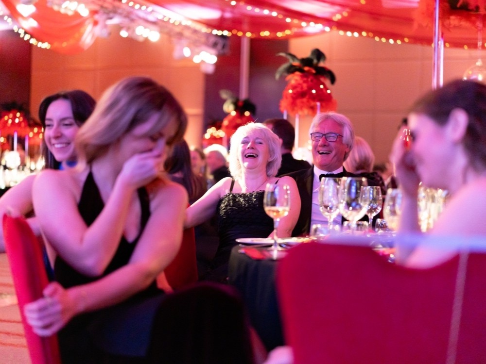 A group of people at the Lily ball laughing and holding their hands over their mouths