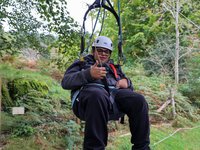 A young man harnessed in a zip wire in trees giving a thumbs up to the camera