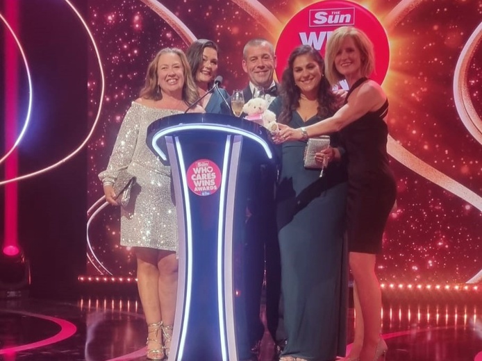 The Lily team behind a podium on stage having been presented with the Sun Who Cares Wins award