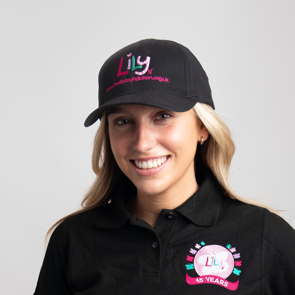 A smiling woman in a black baseball cap featuring the Lily Foundation logo and website address.
