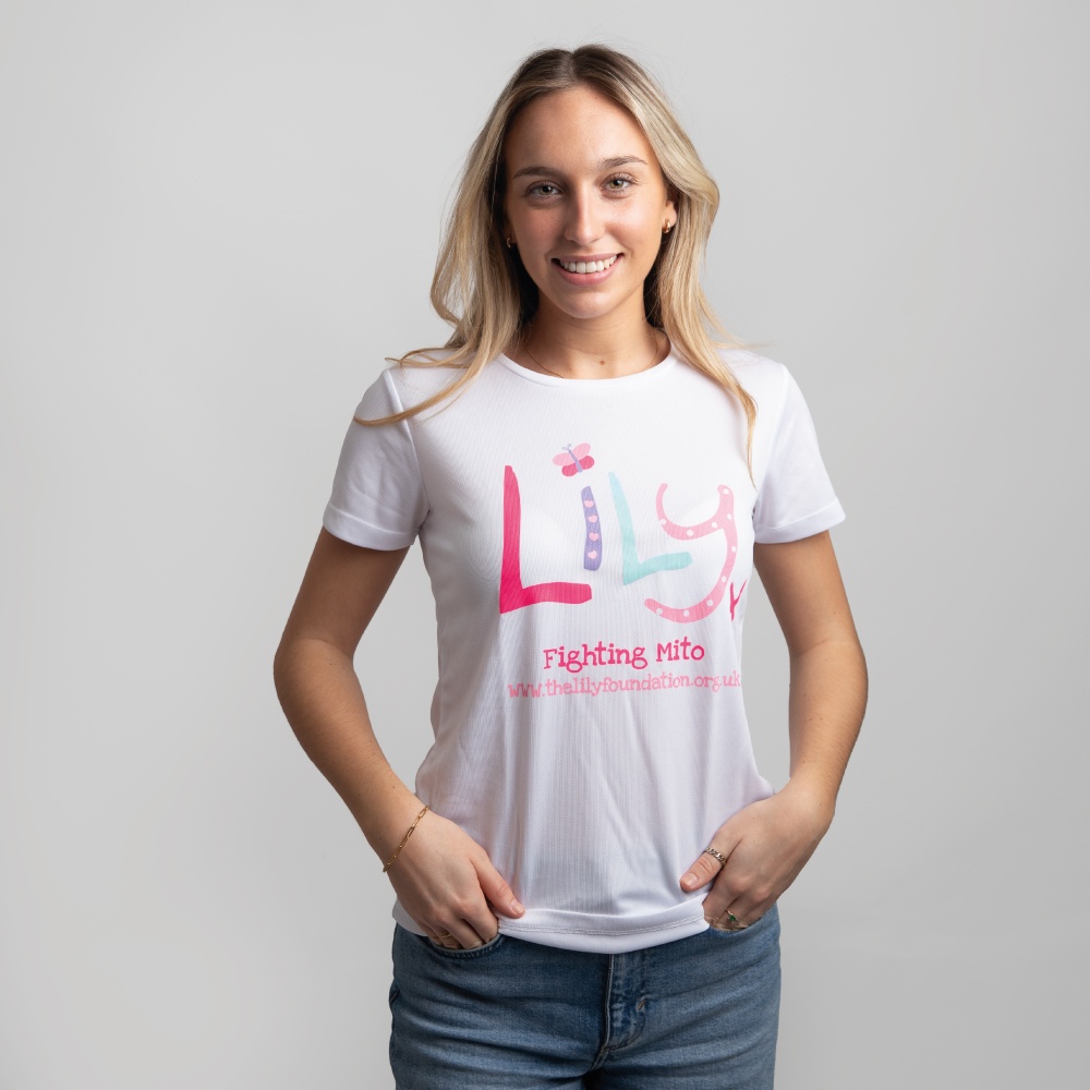 A smiling woman in a white performance t-shirt featuring the Lily Foundation logo and fighting mito underneath.