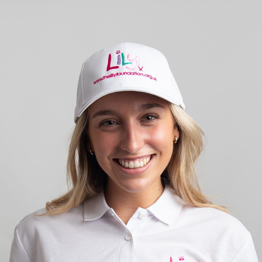 A smiling woman in a white baseball cap featuring the Lily Foundation logo and website address.