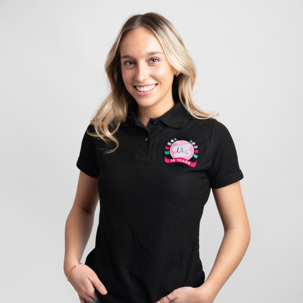 A smiling woman wearing a black polo shirt featuring the Lily Foundation's 15 Years logo on the chest.