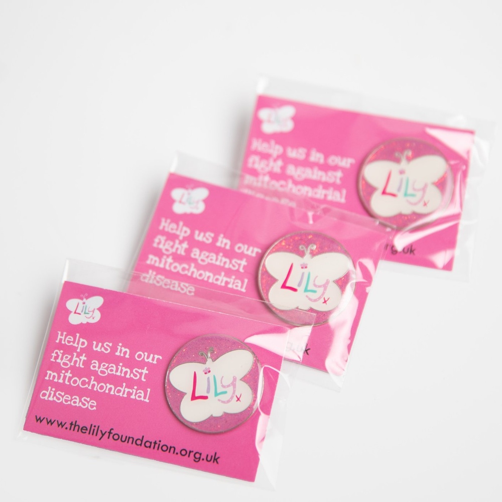Three glittery pink enamel badges featuring the Lily Foundation logo on backing boards.