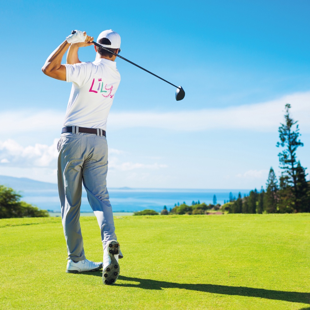 A man in a Lily Foundation top swinging a golf club on the green