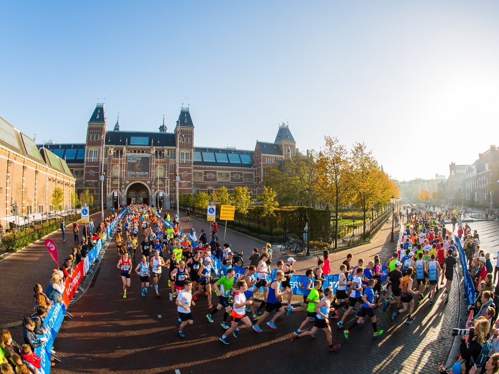 Large group of runners coming down a road and turning a corner onto an Amsterdam canal