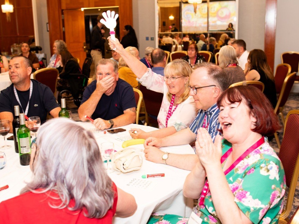A group of people sitting around a table laughing and clapping with papers in front of them