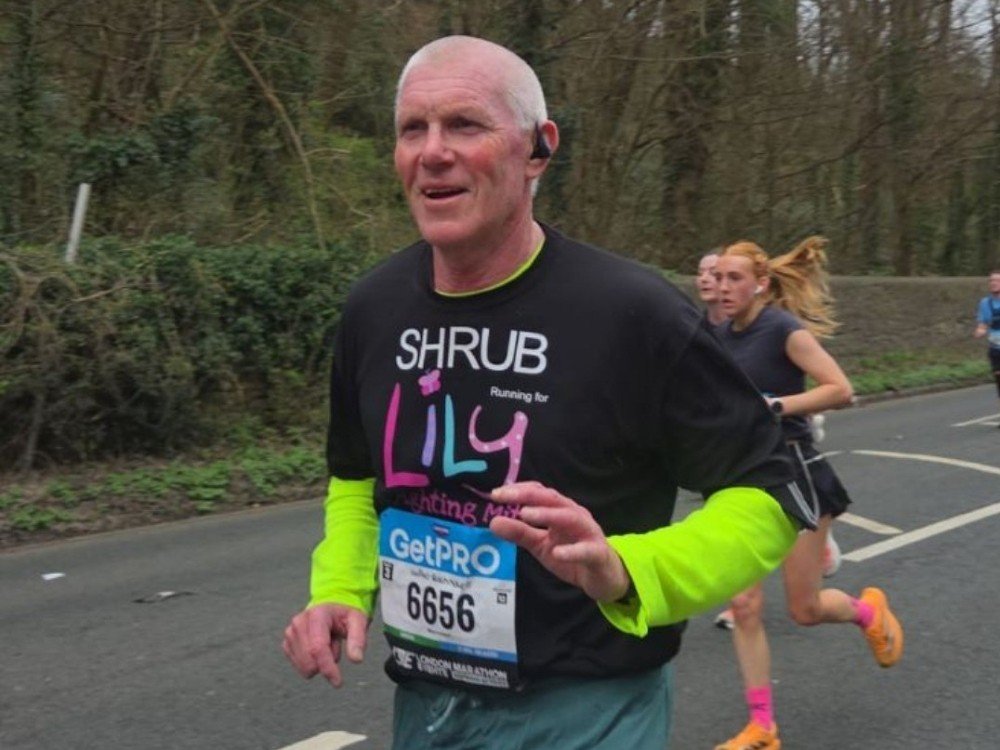 A man running. He has grey hair and is wearing a black Lily t-shirt.