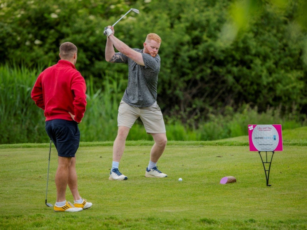 Lily Croham Hurst Golf Day 2027 – Save the Date - Two men on a golf course, one swinging his club and the other watching