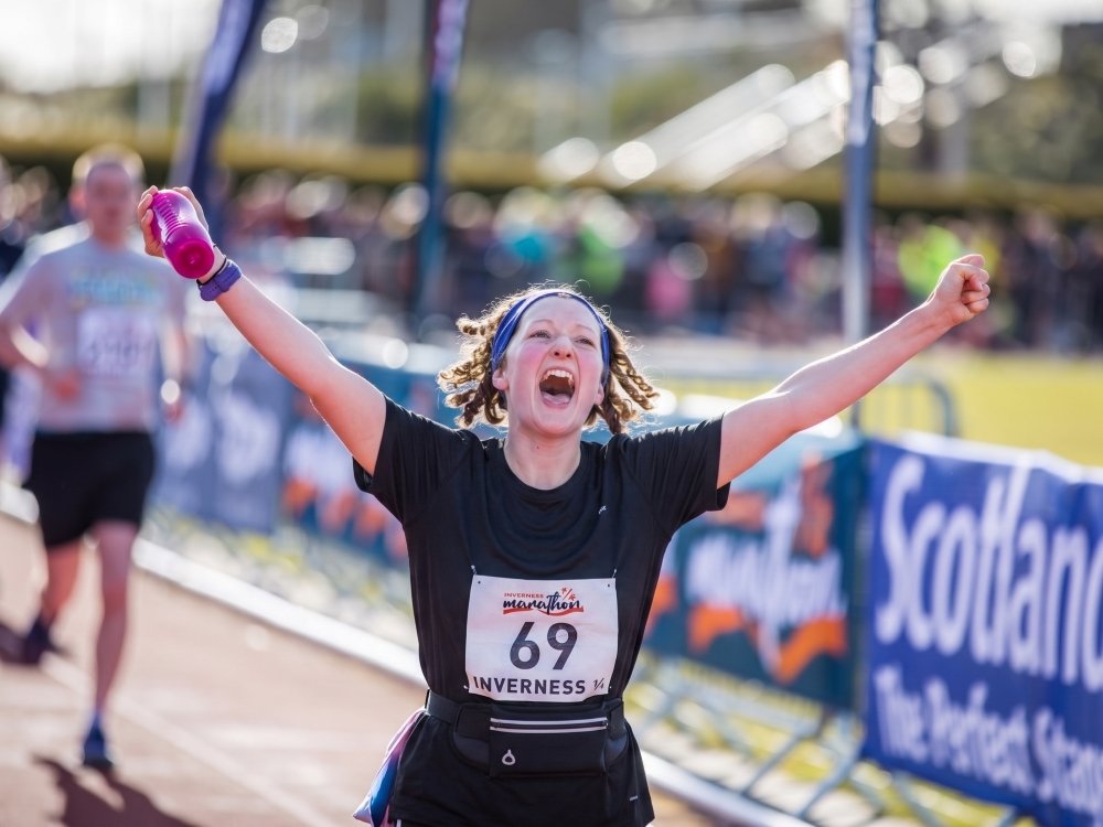 A runner approaching the finish line with arms triumphantly held above her head
