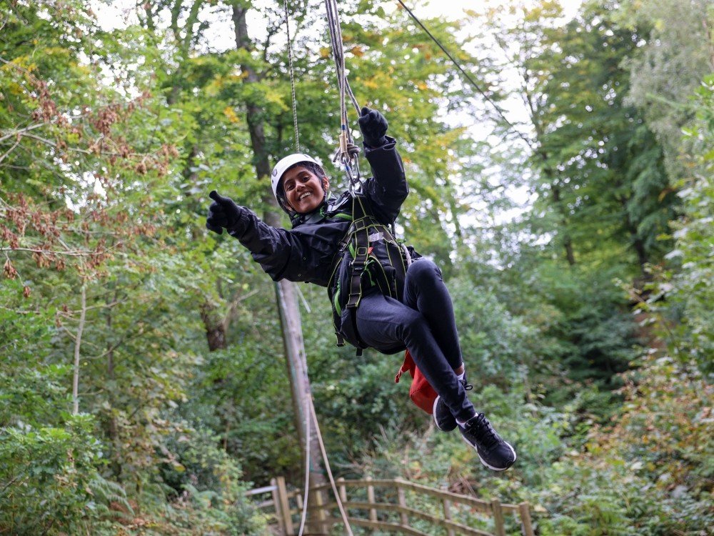 Lily Young Adult Support Weekend 2026 – Save the Date - A young person with mitochondrial disease on a zipwire in trees laughing with her arms in the air