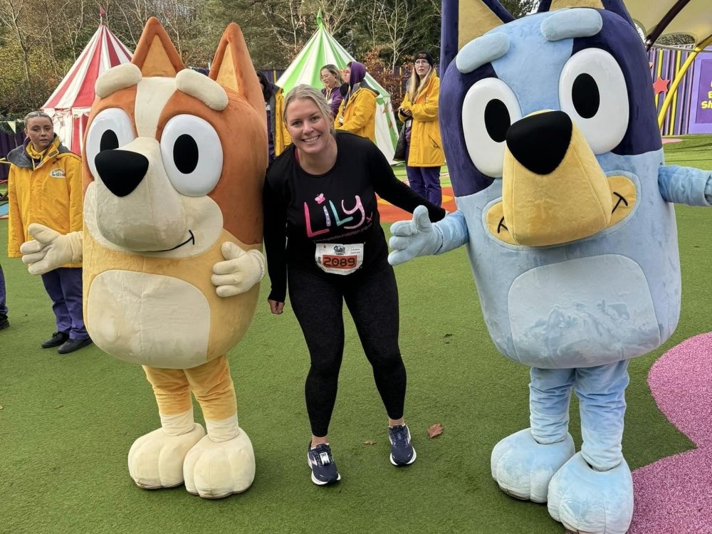 Run Alton Towers 10k 2025 - A lady in a Lily Foundation top laughing and standing between two characters at Alton Towers