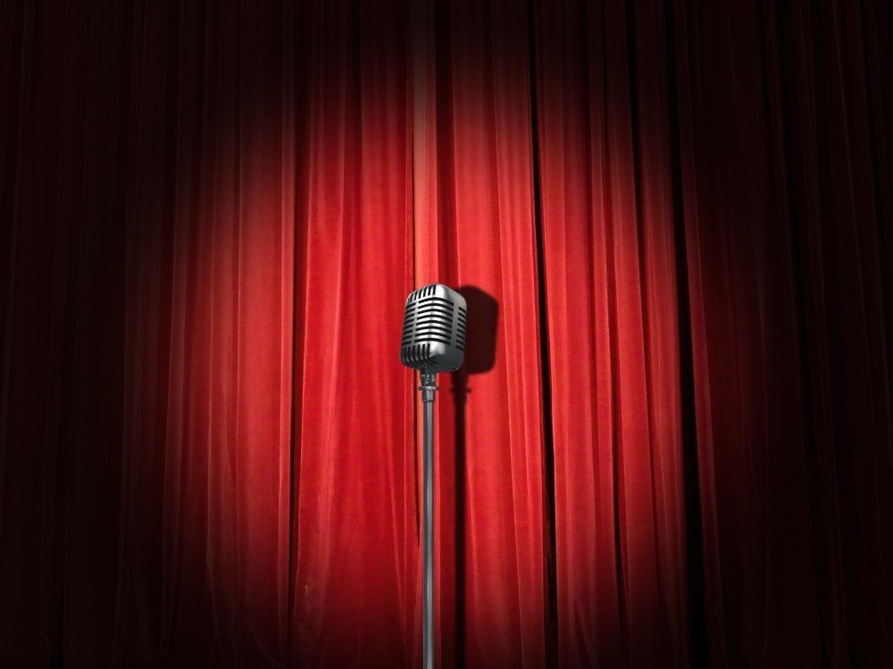 A microphone under a stage spotlight with a red curtain behind