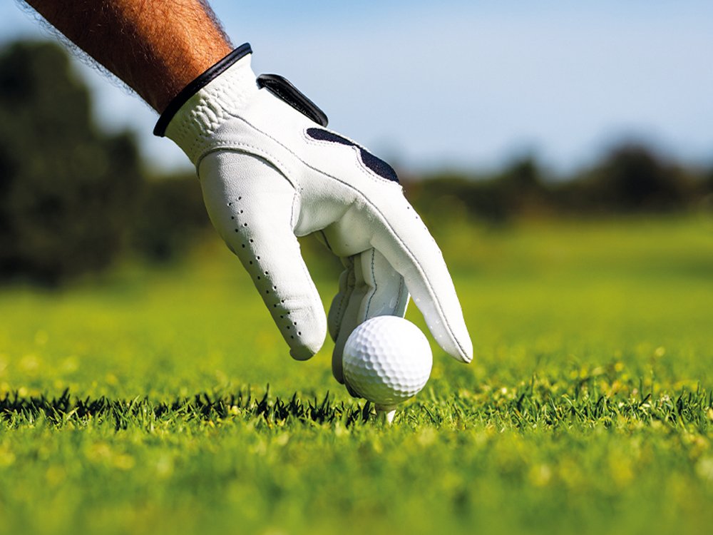 Close-up of a hand in a white glove placing a golf ball onto a tee on the fairway