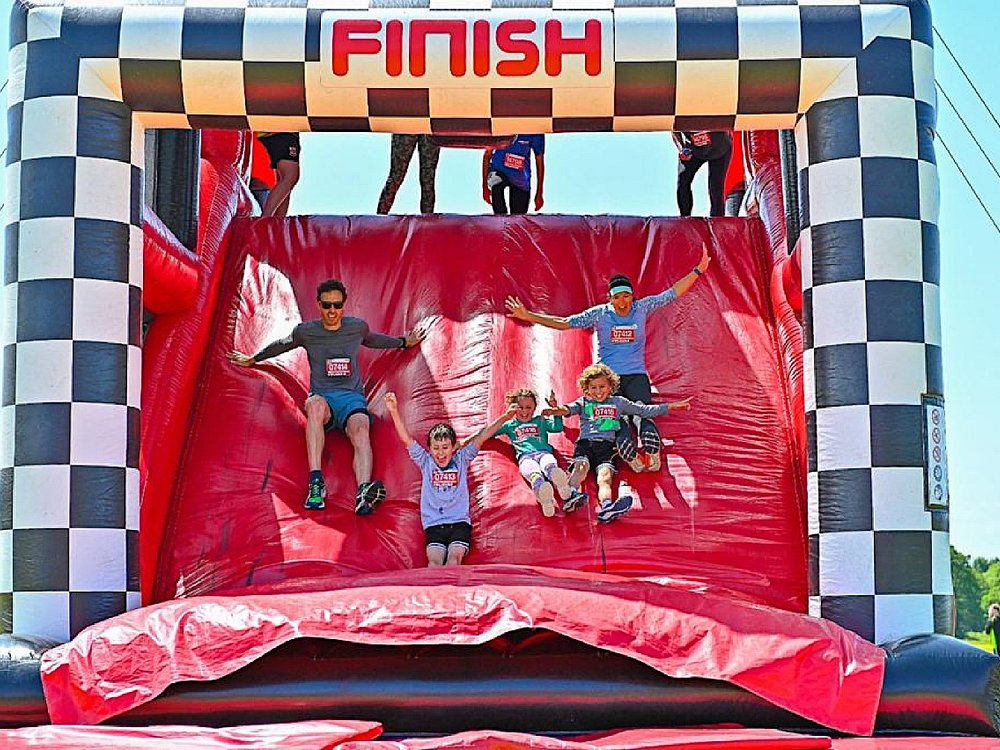 Adults and children with arms raised sliding down a large inflatable finish line slide