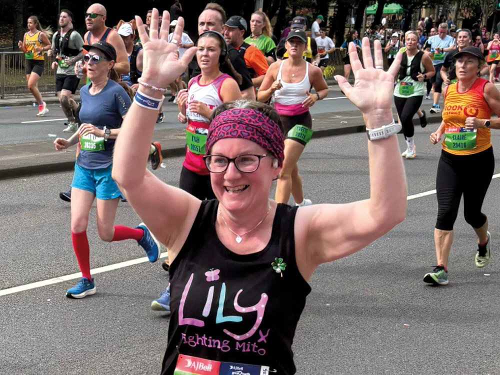 A woman running the Great North Run, wearing a Lily vest, with hands raised triumphantly in the air