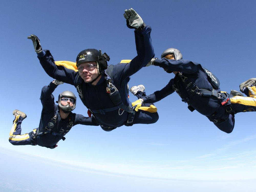 Three people grouped together mid-air on a sky dive with blue sky behind