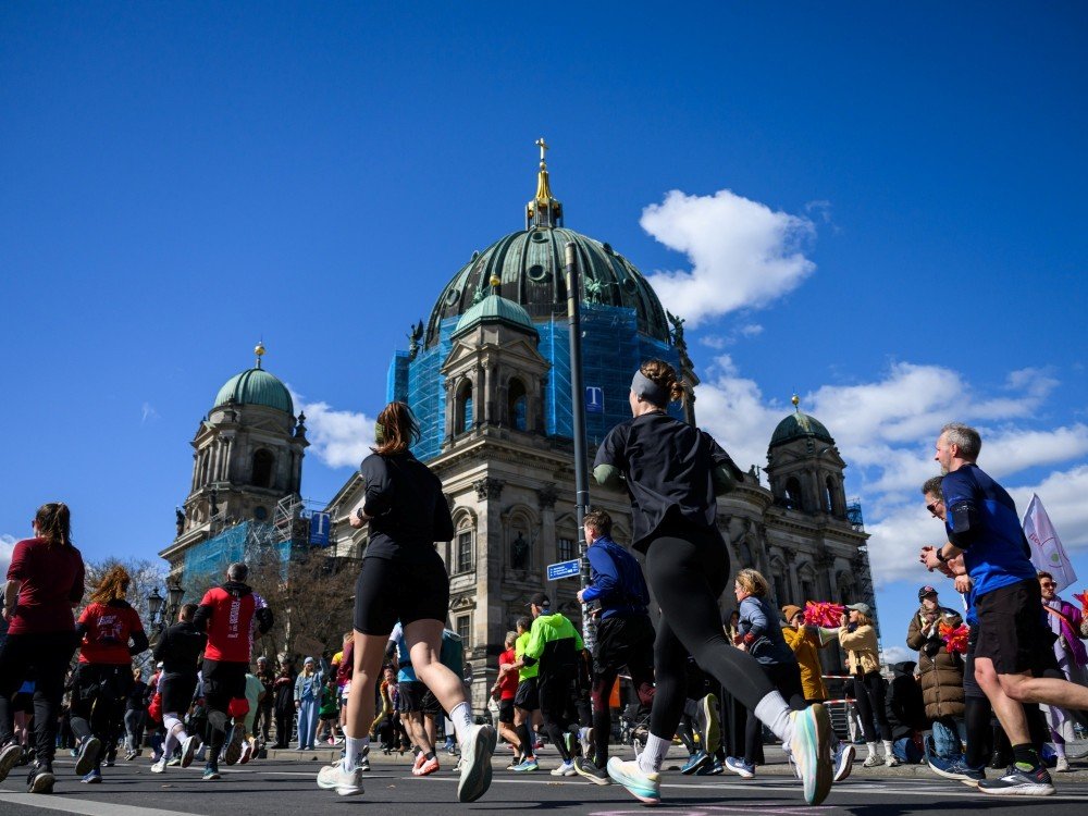 The image shows runners taking part in the Berlin Half Marathon passing the Berlin Cathedral (Berliner Dom), one of the city’s most iconic landmarks.