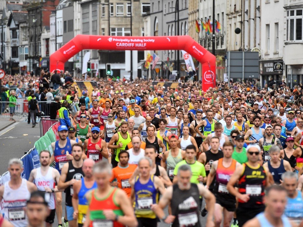 Large number of men and women running through a red inflatable arch that says Cardiff Half Marathon