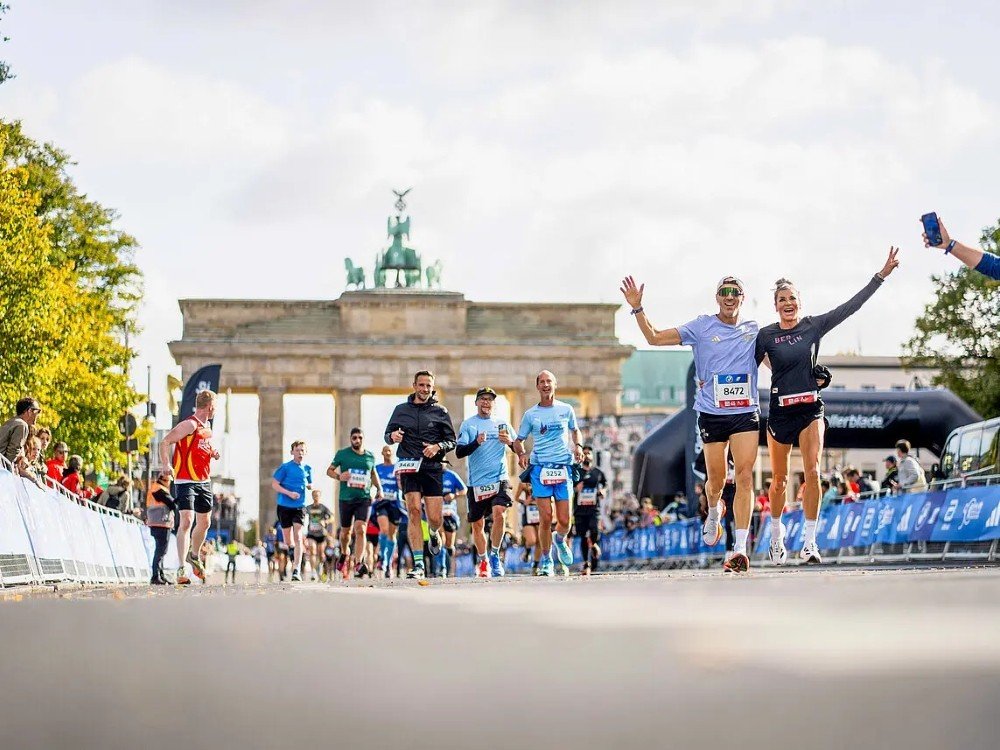 The image shows a group of male and female running with the Brandenburg Gate in the background.