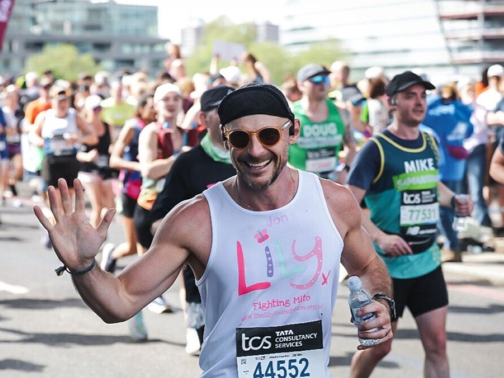 A man in a Lily Foundation vest, wearing a cap and sunglasses and running the London Marathon