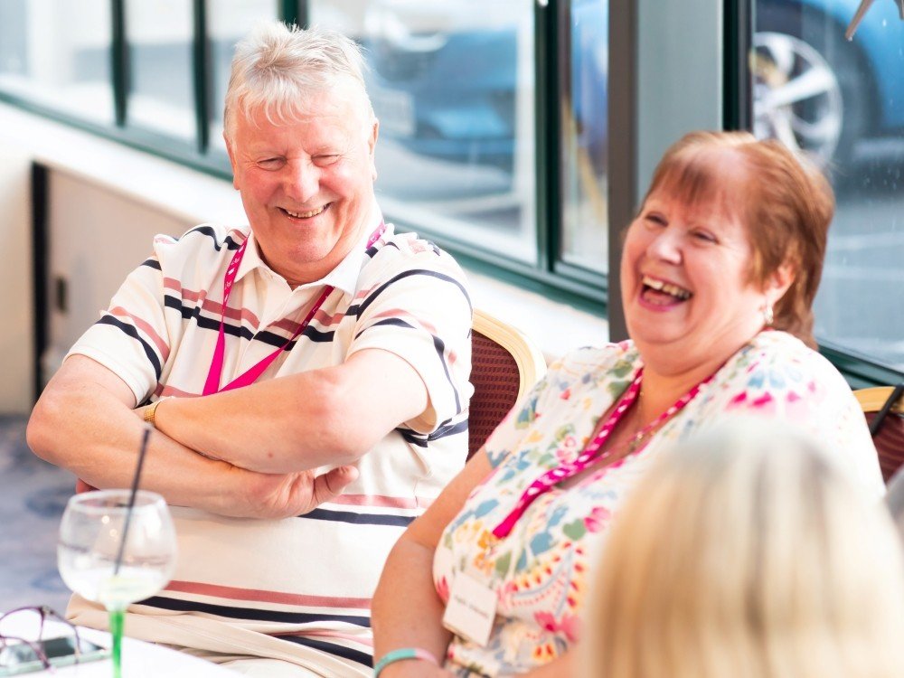 A man and lady laughing at a table at the LIly adult support weekend