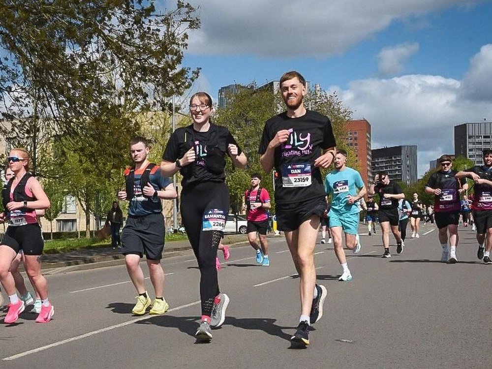 A group of runners approaching the finish line of the Manchester Marathon 2026 including a male and female in black Lily Foundation t-shirts.