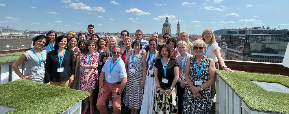 Group of people standing on a roof top in Budapest.. Lovely church can be seen in the distance against a lovely blue sky