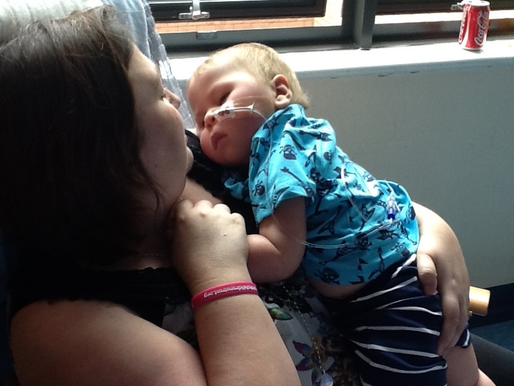 Mother looking lovingly down at her poorly son in her arms
