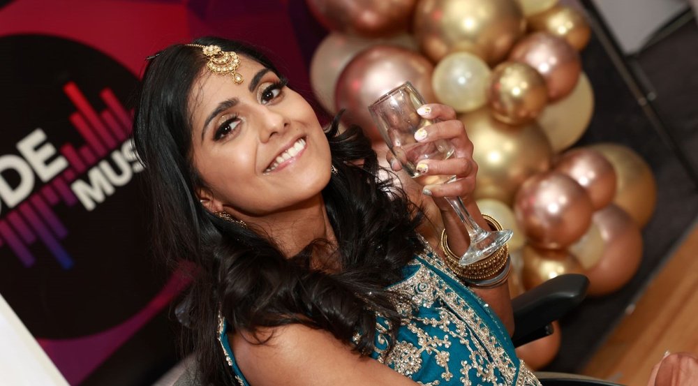 lady with shoulder length brown hair, with gold hair jewellery, holding a glass of champagne