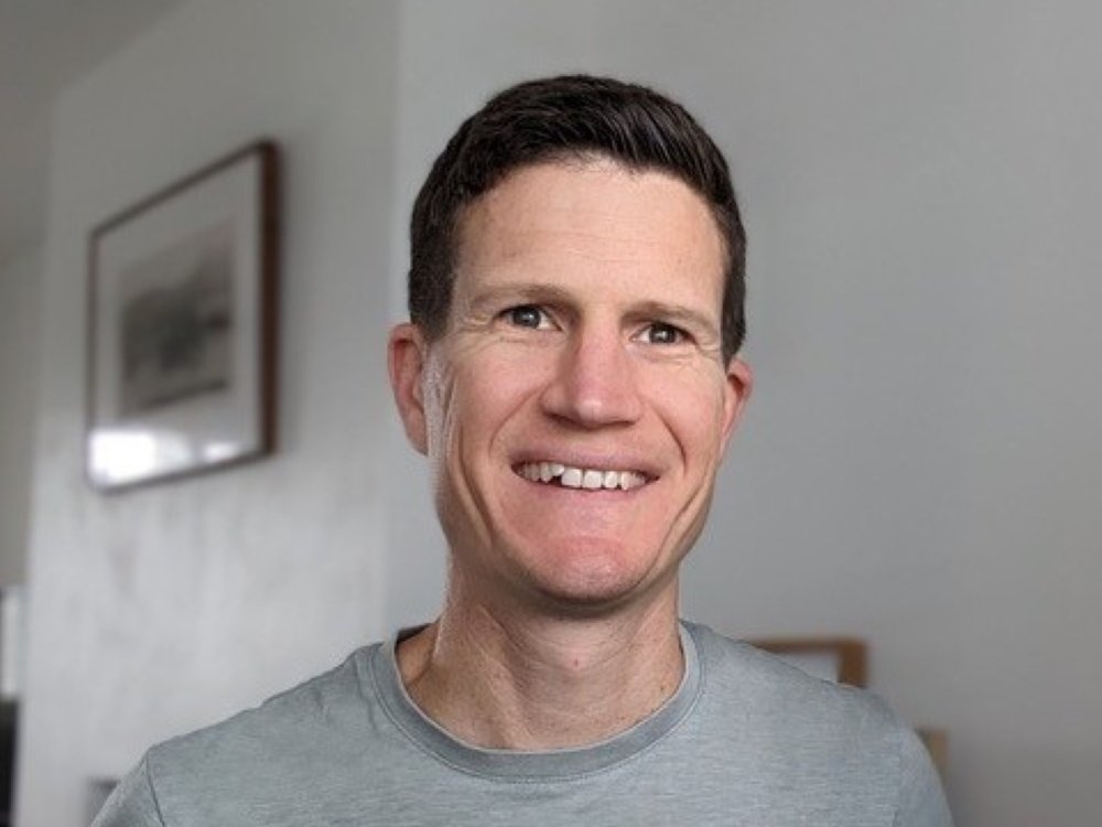 Man with short dark hair and a grey t-shirt smiling