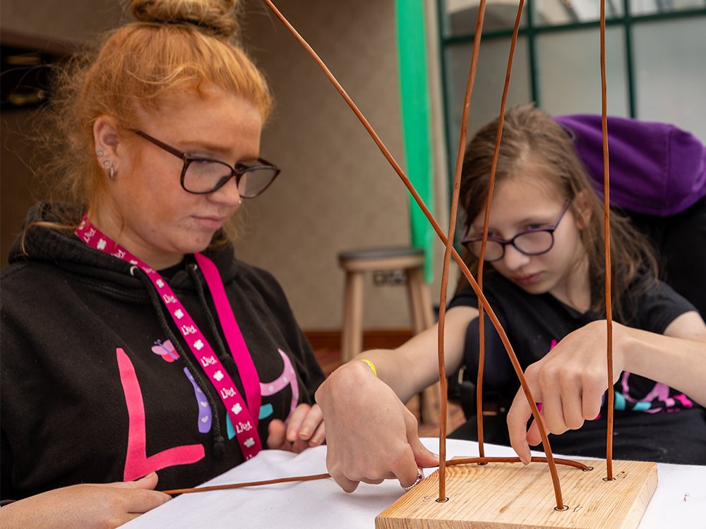 Lily volunteer assisting a young girl with mito to make a wicker basket craft activity