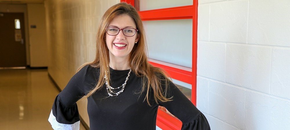 Lady with shoulder length brown hair, in a black top, standing against a red door.