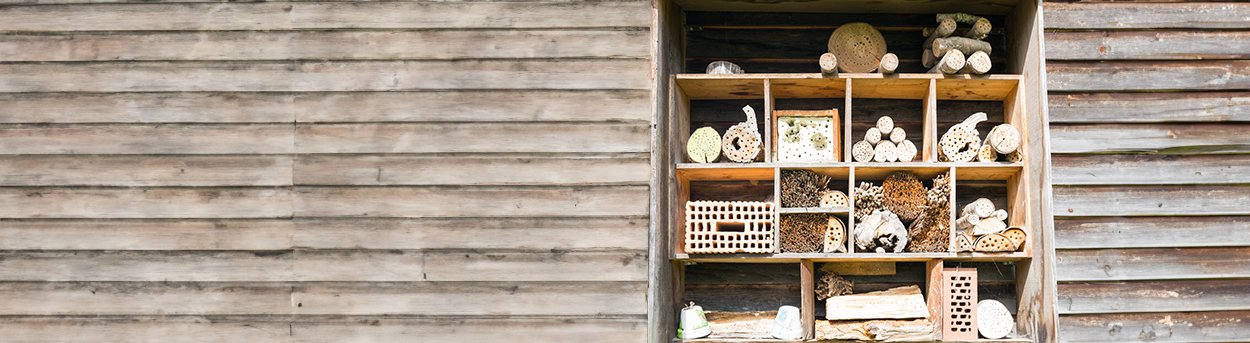 A wooden bug hotel made from a frame which is divided into individual boxes, each packed with interesting logs and sticks