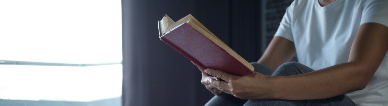 A person sitting in their socks on a bed reading a book