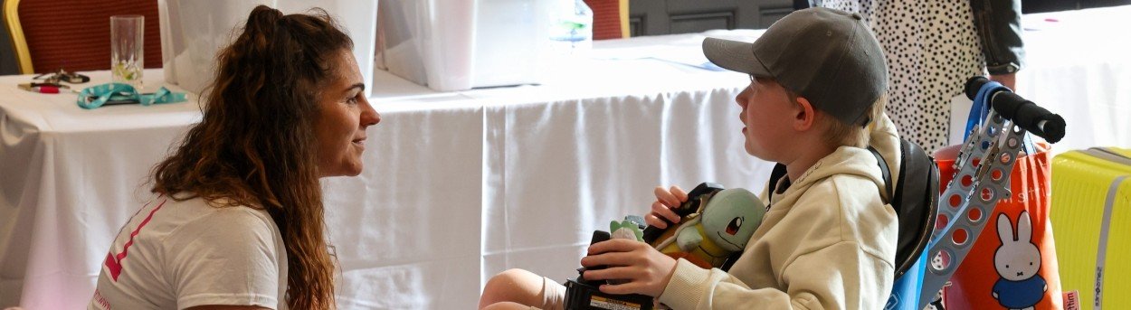 Lily Foundation CEO Liz Curtis kneeling in front of a young mito patient in a wheelchair