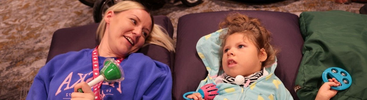 A young TK2d patient lies on the floor next to an adult carer