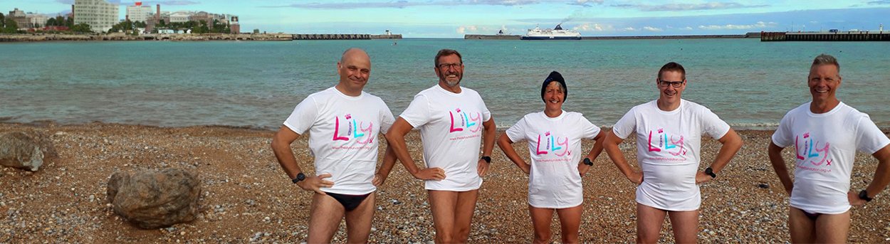 5 Lily fundraisers standing on a pebble beach in  swimming shorts and Lily T-shirts, ready to take the plunge!