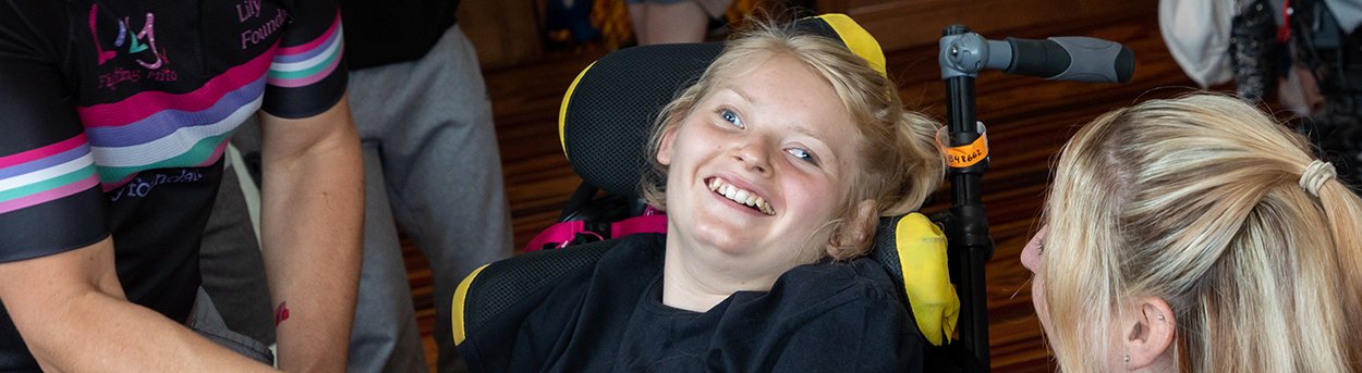 Young girl, who has mitochondrial disease, laughing with her mum and dad from her wheelchair