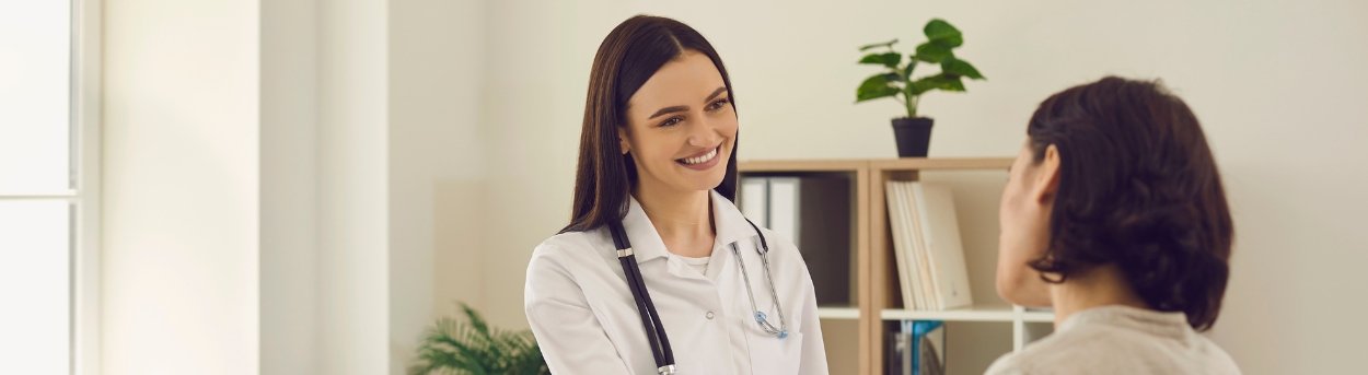 A young female doctor with a stethoscope round her neck smiling and shaking the hand of a female mito patient