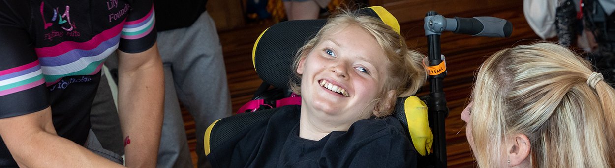 Young girl, who has mitochondrial disease, laughing with her mum and dad from her wheelchair