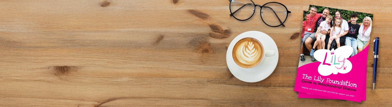 Overhead of the Lily Guide to mitochondrial disease on a table with a coffee cup and pair of glasses