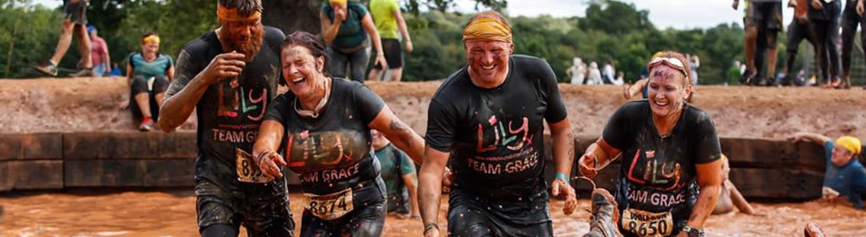 Four Lily Fundraisers, laughing, covered in mud at a Tough Mudder event